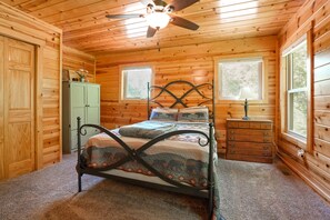 Un dormitorio de cabaña de madera con cama, cómoda y ventanas.