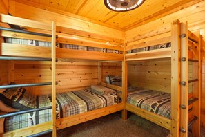 Eine Holzhütte mit Bunkebetten in einer Ecke, jeweils mit Karo-Bettwäsche.