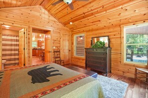 A log cabin bedroom with a bed, dresser, and a window with a view of the outdoors. - Scenic Solitude | Private Pond, Hot Tub, Game Room (Laurelville)