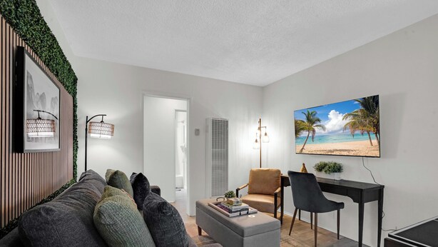 Ein modernes Wohnzimmer mit einem grauen Sofa, einem kleinen Couchtisch, einem Schreibtisch mit zwei Stühlen und einem großen Fernseher im Strandhaus-Stil.