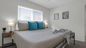 Ein Schlafzimmer mit Bett, Nachttischen, einem Fenster mit Jalousien und zwei gerahmten Bildern an der Wand.
