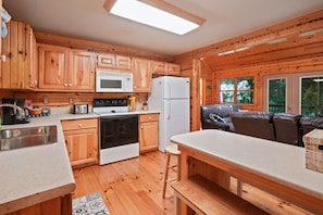 Interior de una cabaña de madera con cocina, comedor y sofá.