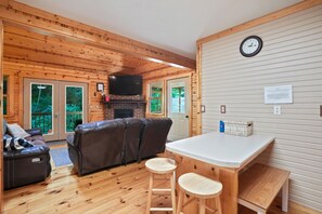 A cozy cabin interior with a wooden floor, a fireplace, a television, and a dining area.
