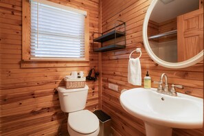Une salle de bain aux murs lambrissés, équipée de toilettes, d’un lavabo et d’un miroir.