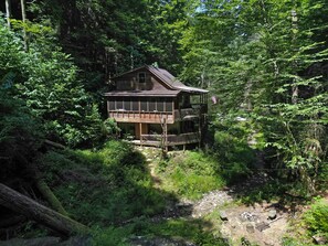 A wooden cabin with a balcony, surrounded by dense forest.