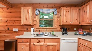 A kitchen with wooden cabinets, a dishwasher, and a window with a view of greenery. - Hidden Falls Retreat | Hocking Hills, Waterfall (Rockbridge)