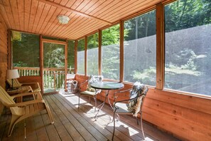 Une terrasse en bois avec une table et des chaises, de grandes fenêtres et une vue sur la forêt.