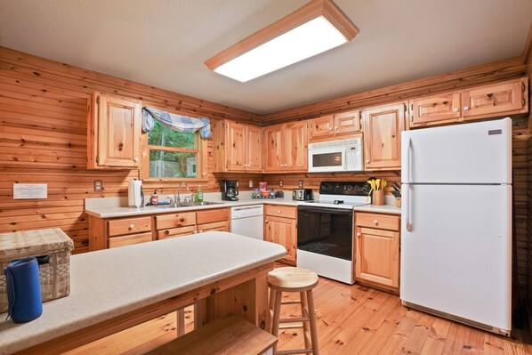 Una cocina con gabinetes de madera, un refrigerador blanco, un microondas, una estufa y un lavamanos.