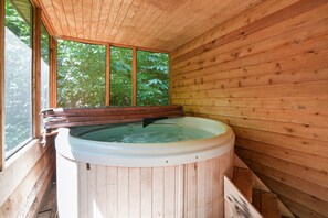 Una baita di legno con vasca idromassaggio, ampie finestre e vista sul verde.