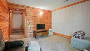 A cozy room with a wooden wall, a television on a wooden stand, a sofa, a small table, and a staircase leading to another area. - Hidden Falls Retreat | Hocking Hills, Waterfall (Rockbridge)