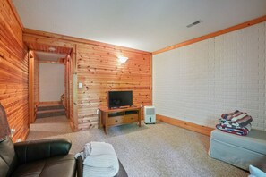 A cozy room with a wooden wall, a television on a wooden stand, a sofa, a small table, and a staircase leading to another area.