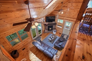 Interior de una cabaña de madera con sofá, chimenea, televisión y ventilador de techo.