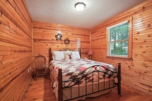 Un dormitorio tipo cabaña de madera con una cama, una silla y un ventanal.