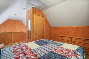 A bedroom with a wooden wardrobe, a quilted bedspread, and a sloped ceiling.