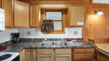 Una cocina con gabinetes de madera, encimera de granito, pileta doble, estufa y comedor con mesa y sillas.