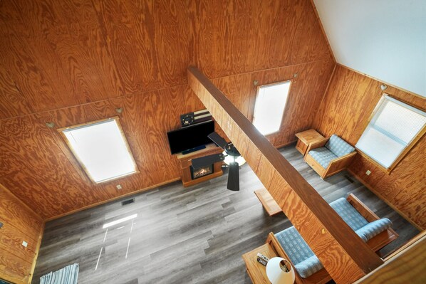 Una habitación pequeña y acogedora, con piso de madera, televisor, zona de estar y dos ventanas.