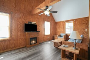 A wooden-paneled room with a fireplace, a ceiling fan, a television, and a sofa with a lamp. - Retreat Cabin #4 | Hocking Hills,  Pet Friendly (Logan)