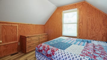 Un dormitorio con un aparador de madera, colcha acolchada y ventana con persianas.