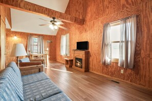 Una sala de estar acogedora con chimenea, paredes de madera, un sofá, un televisor y un ventilador de techo.