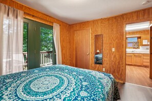 Un dormitorio con una cama grande, paredes de madera, una puerta verde y vistas al exterior.
