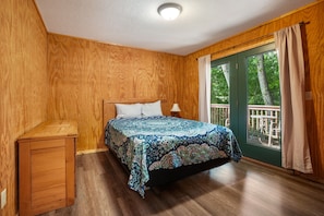 Ein Schlafzimmer mit Holzboden, einem Bett mit gemustertem Überwurf, einem Nachttisch und einem Fenster mit Vorhängen.