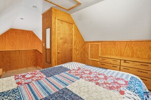 A bedroom with a wooden wardrobe, a quilted bedspread, and a sloped ceiling.