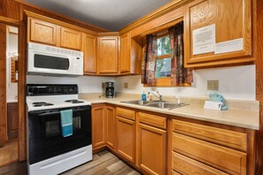 A kitchen with wooden cabinets, a microwave, stove, sink, and a window with curtains.