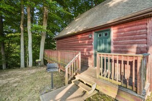 Une cabane rustique en rondins de bois, avec une porte verte, des marches en bois et un petit porche.