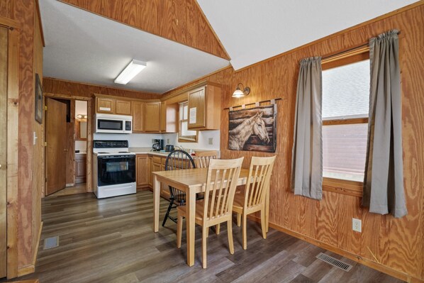 A wooden interior with a kitchen, dining table, and chairs. - Retreat Cabin #3 | Hocking Hills, Loft Cabin (Logan)