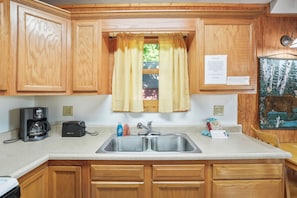 A kitchen with wooden cabinets, a double sink, a coffee maker, and a toaster.