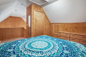 Une chambre avec une armoire en bois, un lit recouvert d’une couvre-lit à motifs et une commode en bois.