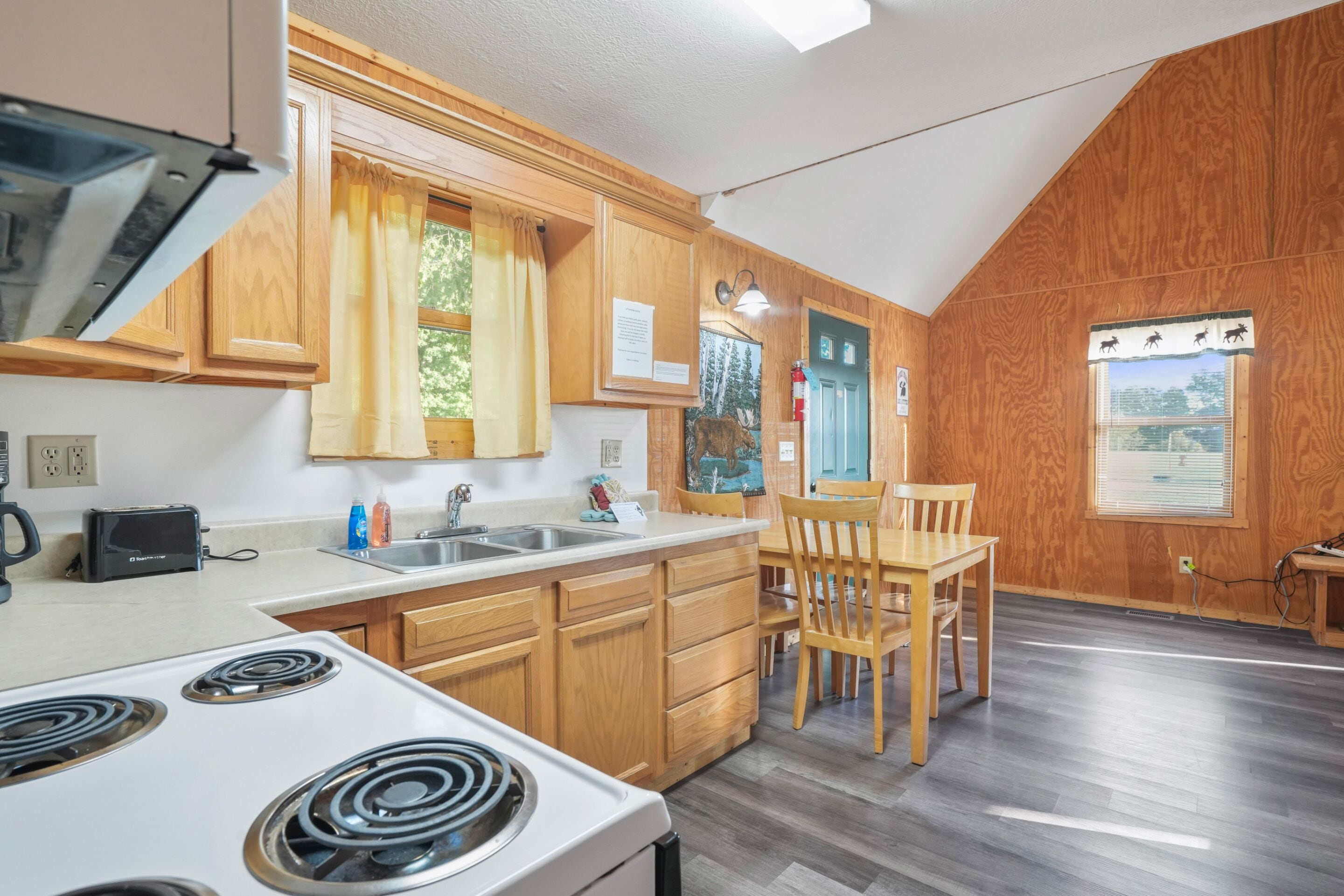 A kitchen with wooden cabinets, a white stove, a sink, and a dining area with a table and chairs.