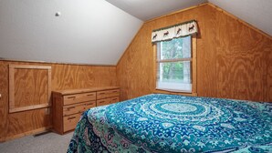 Un dormitorio con techo de madera, una ventana con persianas, una cama con colcha estampada y un aparador de madera.