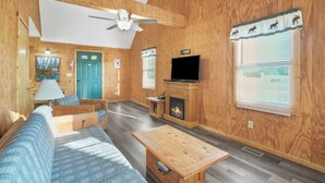 Una sala de estar con detalles de madera, un sofá, una mesa de centro, una chimenea, un televisor y un ventilador de techo.