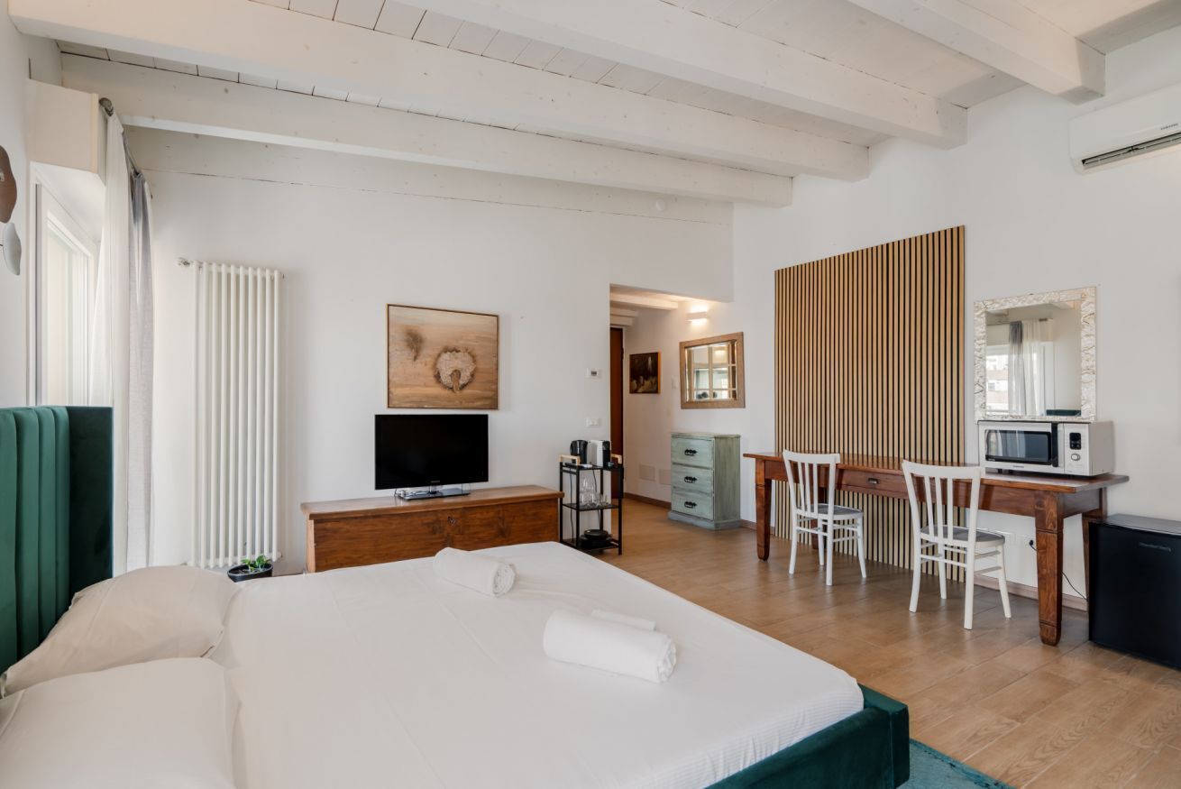 A modern hotel room with a bed, a TV, a desk with a chair, a microwave, and a wooden panel wall.