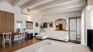 A modern hotel room with a bed, a white sofa, a desk with a chair, a mirror, and a television.