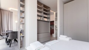 A modern hotel room with a bed, a seating area with chairs, a dining table, and built-in shelving. - GuestHost - Porta Venezia - Modern Studio near Corso Buenos! (Milano)