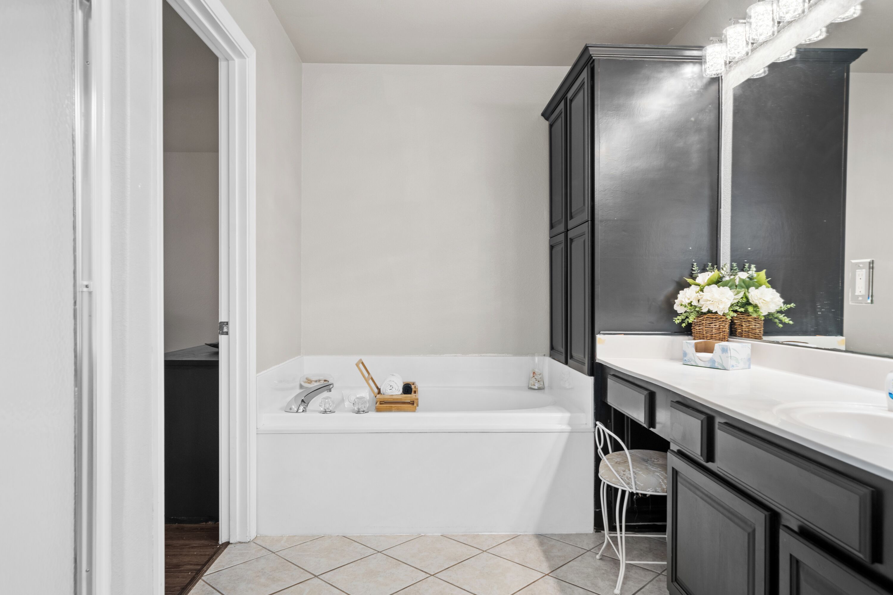 A modern bathroom with a white bathtub, dark cabinetry, and a large mirror.
