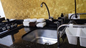 A kitchen with a stainless steel sink, black granite countertops, a gas stove, and a gold-patterned backsplash. - Renomado Apartamento em Curitiba  (Curitiba)