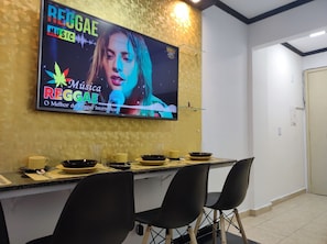 A dining area with a TV displaying a music event, a table set with bowls and cups, and two chairs.