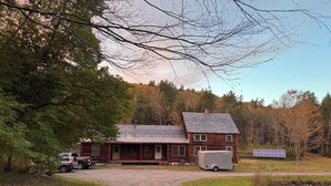 Un rustico chalet con vialetto sterrato, un camion parcheggiato e un pannello solare.