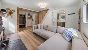 A modern living room with a large beige sectional sofa, wooden flooring, and a staircase leading to a kitchen area.