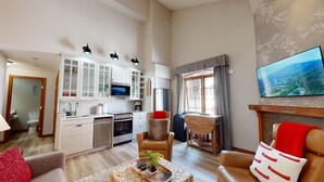 Una sala de estar moderna con chimenea, televisor y un área de cocina con armarios y electrodomésticos.
