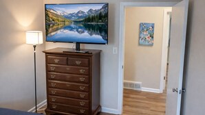 Une chambre à coucher avec une télévision posée sur une commode, une lampe et une porte donnant sur une autre pièce.