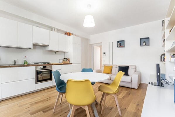 A modern kitchen with white cabinets, a stove, and a dining area with a round table and chairs.