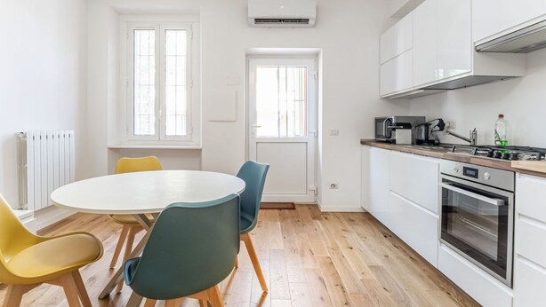 Een moderne keuken met witte kasten, een ronde eettafel met stoelen en een oven.