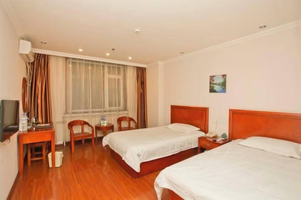 A hotel room with two beds, a desk with a chair, a small table, a television, and a window with curtains.