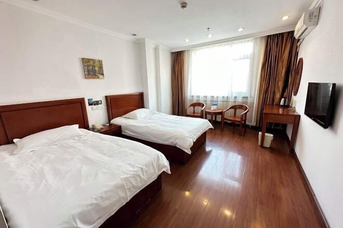 A hotel room with two beds, a desk, a chair, a TV, and a window with curtains.