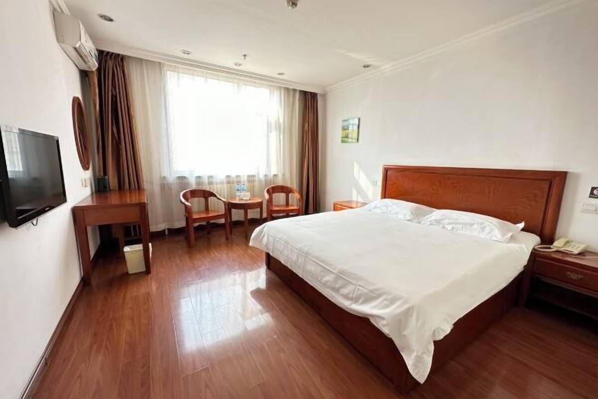 A hotel room with a bed, a desk, a chair, a TV, and a window with curtains.