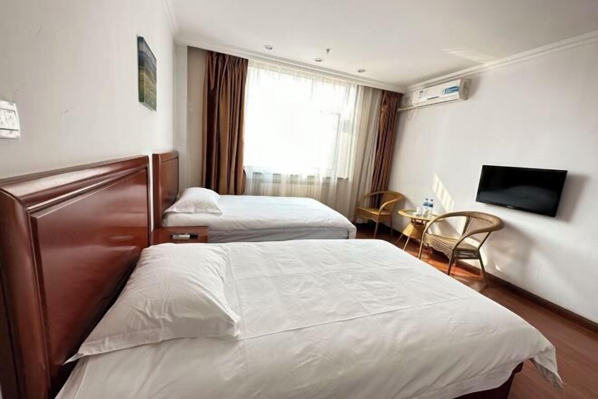 A hotel room with two beds, a television, a chair, and a window with curtains.